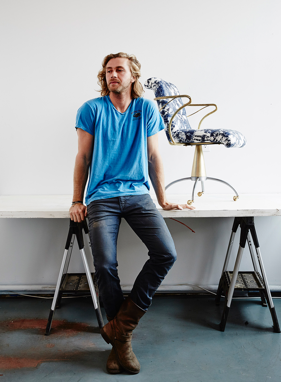 Cam Crockford leans casually against a desk, with a modern chair of his own design positioned next to him.
